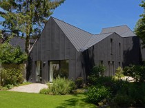 Une maison noire s'immisce entre les arbres et la ...