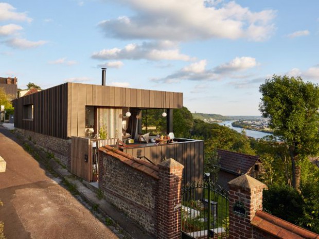 Une maison en zinc noir posée sur un mur en brique