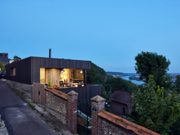 Une maison en zinc noir posée sur un mur en brique