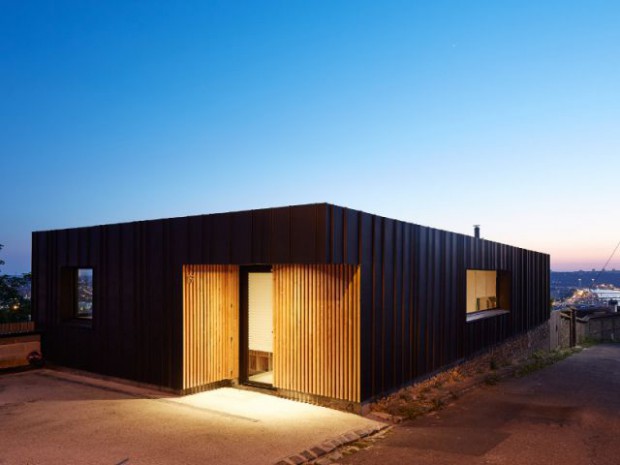 Une maison en zinc noir posée sur un mur en brique