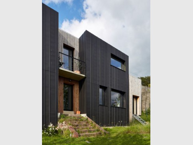 Une maison en zinc noir posée sur un mur en brique