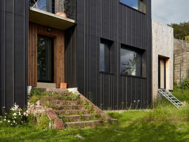 Une maison en zinc noir posée sur un mur en brique